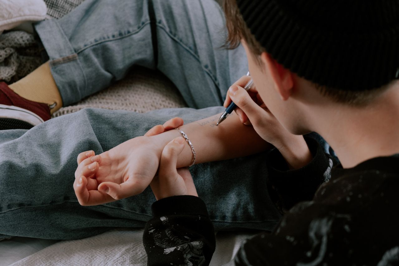 Young individual writing on their forearm with a pen, wearing casual clothing.